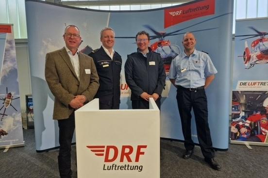 4 Männer stehen vor Werbeplakat der Deutschen Luftrettung in einer Halle
