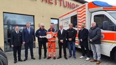 Übergabe Symbolisch mit großem Schlüssel vor der Wache. Mehrere Personen stehen am RTW