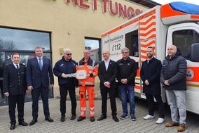 Übergabe Symbolisch mit großem Schlüssel vor der Wache. Mehrere Personen stehen am RTW