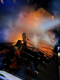 Löscharbeiten von oben. Man kann deutlich Flammen und Rauch sehen und blickt durch das Dach.