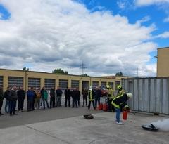 Mehrere Menschen stehen und schauen, wie eine Person mit deinem Feuerlöscher einen Brand in einer Feuerschale löscht.