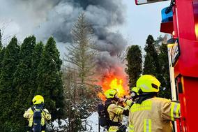 Feuerwehrmänner am Fahrzeug im Hintergrund Flammen.