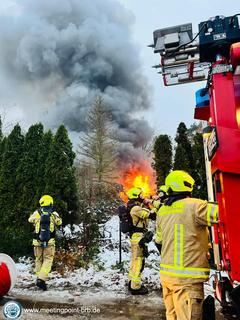 Feuerwehrmänner am Fahrzeug im Hintergrund Flammen.