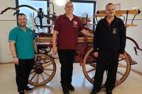 3 Männer vor einer alten Löschkutsche