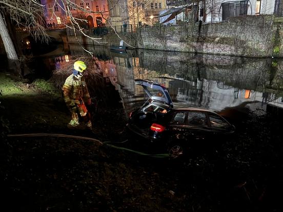 Auto im Wasser an Seilwinde. Daneben ein Feuerwehrmann