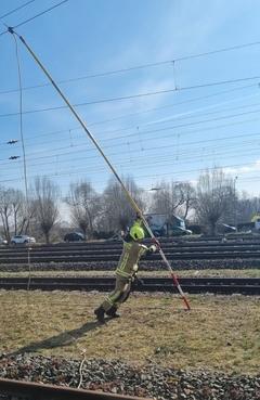 Feuerwehrmann hat eine lange Stange in der Hand, die er zu Oberleitung der Bahn führt