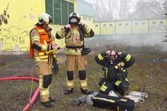 Feuerwehrmänner ziehen sich draußen Pressluftatmer an. Im Hintergrund qualmt es.