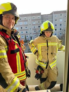 Ein Feuerwehrmann und eine Feuerwehrfrau stehen auf dem Balkon. Die Sonne scheint.