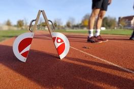 Startblock auf einer roten Tartanbahn, im Hintergrund Beine