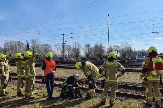 Feuerwehrmänner stehen an Bahngleisen und üben Bahnerden