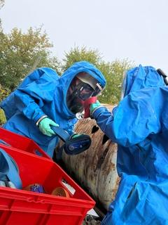 zwei Männer in blauen Schutzanzügen am Chemiefass