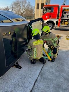 Feuerwehrmänner bei der Übung am Schrottauto. Im Hintergrund ein Feuerwehrfahrzeug.