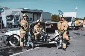 Gruppenbild am kaputten Fahrzeug mit Geräten in den Händen