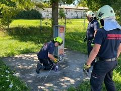 Ein Feuerwehrmann befestigt ein Zugseil, zwei andere sehen dabei zu