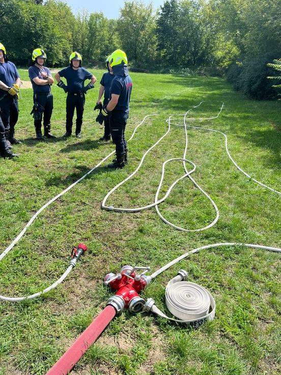 Im Fordergrund eine Kupplung mit Schläuche. Im Hintergrund stehen Einsatzkräfte