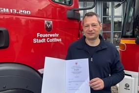 Unser Kollege mit seinem Zeugnis vor einem Fahrzeug