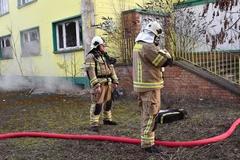 Rauch aus Kellerfenster, davor zwei Feuerwehrmänner und ein Schlauch.