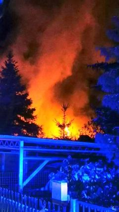 Rauchwolke mit roten Flammen. Davor ein Zaun.