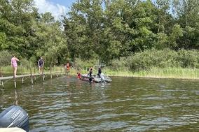Bild vom Wasser aus auf einen Steg gerichtet. Auf dem Steg sind Personen und es befindet sich ein Rettungsboot auf dem Wasser