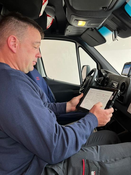 Mitarbeiter der Feuerwehr mit dem neuen Tablet in der Hand im Auto.