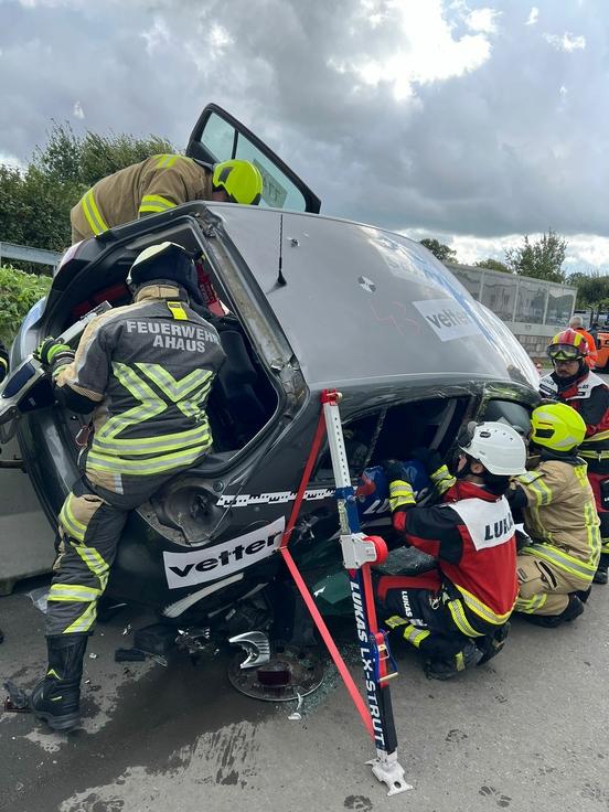 Auto steht schräg und Feuerwehrmänner über daran