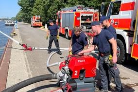 Feuerwehrmänner an der Tragkraftspritze. Im Hintergrund Einsatzfahrzeuge