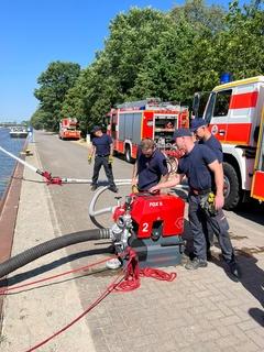 Feuerwehrmänner an der Tragkraftspritze. Im Hintergrund Einsatzfahrzeuge