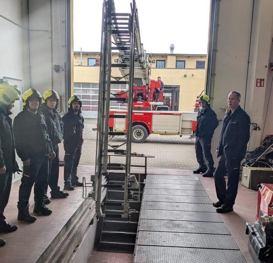 Mitarbeiter der Feuerwehr in der Fahrzeughalle. Die Drehleiter steht davor.