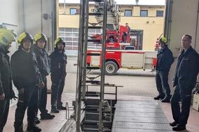 Mitarbeiter der Feuerwehr in der Fahrzeughalle. Die Drehleiter steht davor.