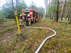 Feuerwehrschläuche im Vordergrund und 3 Feuerwehrläute am Auto in Hintergrund