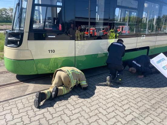 Drei Feuerwehrleute sind am Boden und schauen unter die Bahn