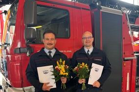 Zwei Kollegen mit Blumenstrauß und Zeugnissen vor einem Feuerwehrauto