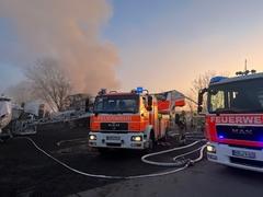 Löschfahrzeuge und Schläuche im Vordergrund, dahinter Qualm und das Boot
