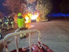 Brennende Autos davor Feuerwehrmänner