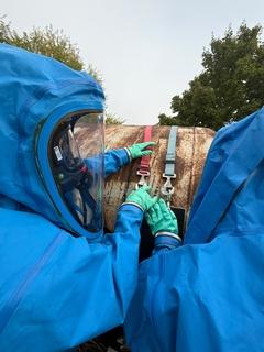 zwei Männer in blauen Schutzanzügen am Chemiefass