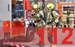 Feuerwehrautos und Männer im Hintergrund. Davor groß und fett die 112