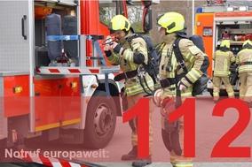 Feuerwehrautos und Männer im Hintergrund. Davor groß und fett die 112