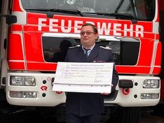 Kamerad am Feuerwehrauto mit Scheck in den Händen
