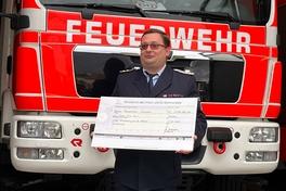 Kamerad am Feuerwehrauto mit Scheck in den Händen