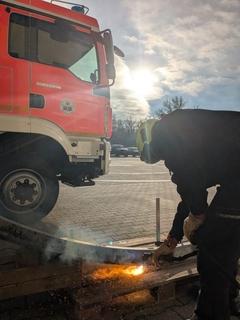 Arbeiten mit dem Plasmaschneider, es sind Funken zu sehen, eine Feuerwehrmann sowie das Fahrzeug sind auch auf dem Bild