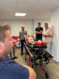 Trage mit einer Kinderpuppe. Drumherum stehen Personen