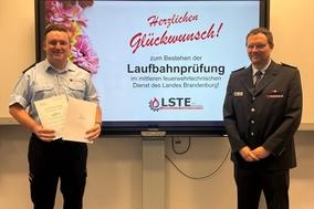 Philipp und Hendrik vor einem Bildschirm. Philipp hält seine Urkunde.