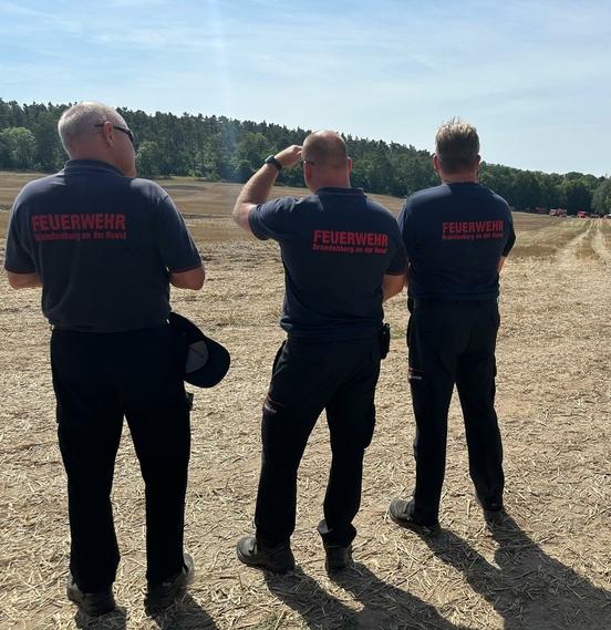 3 Mitarbeiter der Feuerwehr Brandenburg auf einem Feld zur Übung