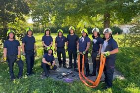 Feuerwehrmänner posieren für Gruppenfoto unter bäumen. Zwei halten einen Schlauch.