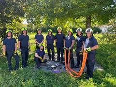 Feuerwehrmänner posieren für Gruppenfoto unter bäumen. Zwei halten einen Schlauch.