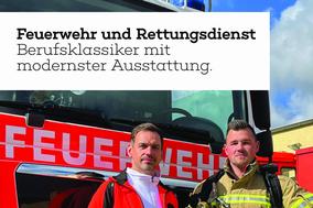 Vor einem Feuerwehrfahrzeug stehen zwei Männer. Einer trägt Rettungsdienstbekleidung und der andere ist Feuerwehrmann