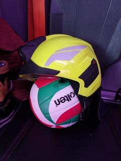 Ein Volleyball hat einen Feuerwehrhelm auf. Beides liegt auf einem Sitz im Auto.