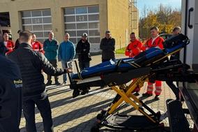 Mitarbeiter stehen draußen am RTW und bekommen die Trage vorgestellt