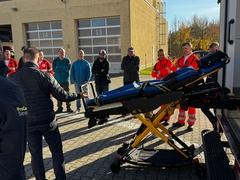 Mitarbeiter stehen draußen am RTW und bekommen die Trage vorgestellt