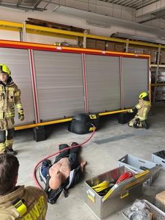 Container der Feuerwehr. Davor eine Puppe und drei Feuerwehrmänner die üben.